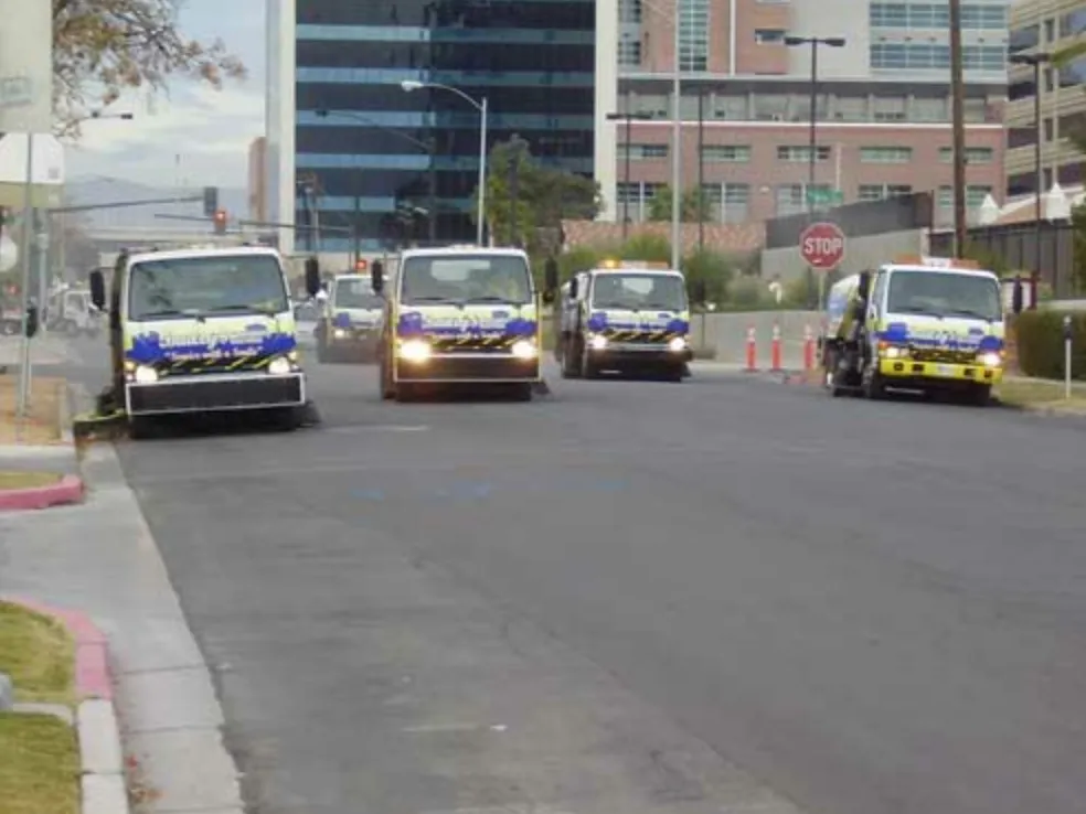 Four Bailey's sweeper trucks driving in convoy through downtown Las Vegas