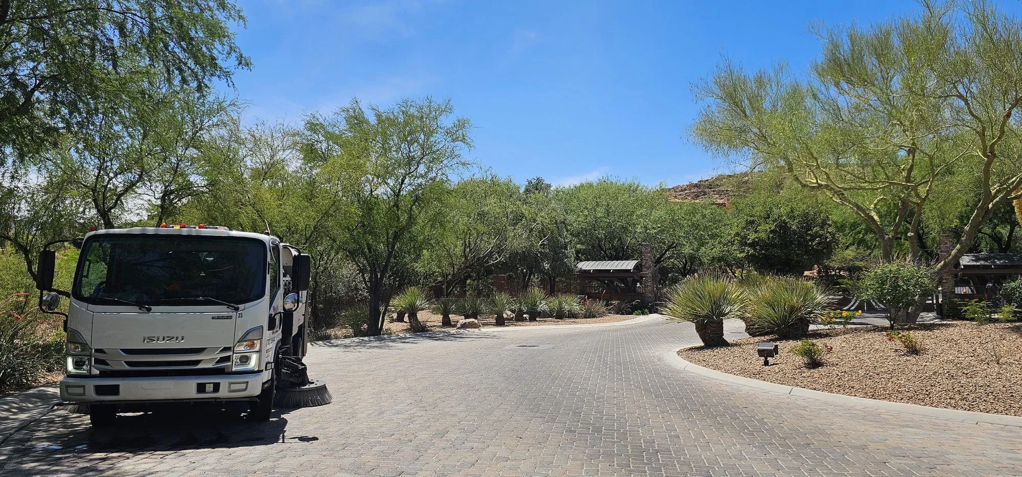 Front view of a Bailey's sweeper on a paver street with a desert estate in the background