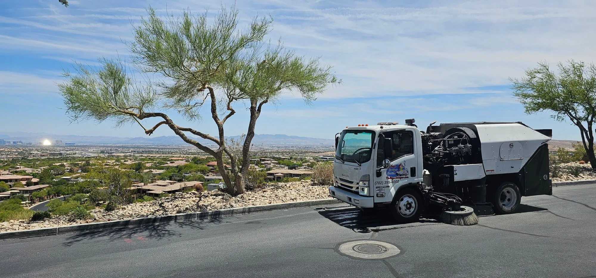 Bailey's sweeper truck on a hilltop road at The Ridges with the Las Vegas Strip and desert valley in the distance